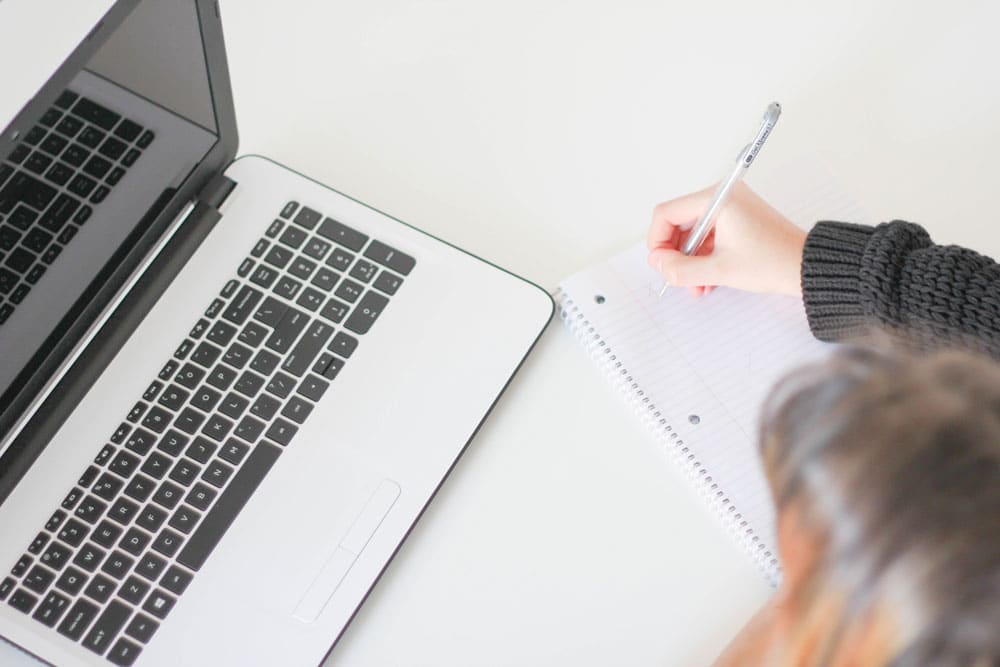 A girl writing a checklist, next to a computer.